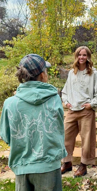 Back of the Unbroken Moose hoodie with the hood up, styled next to the Get Lost hoodie
